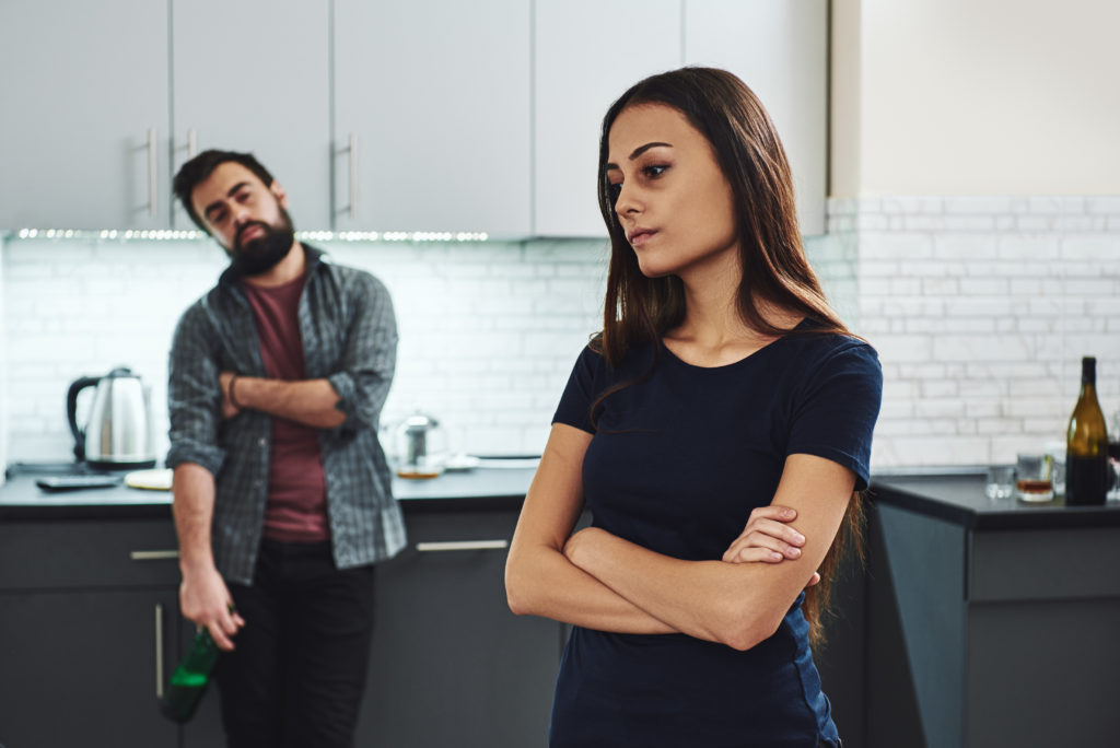 woman stands with her arms crossed. Man appears antagonistic with a bottle hanging in his hand, which may be a red flag this is an unhealthy relationship